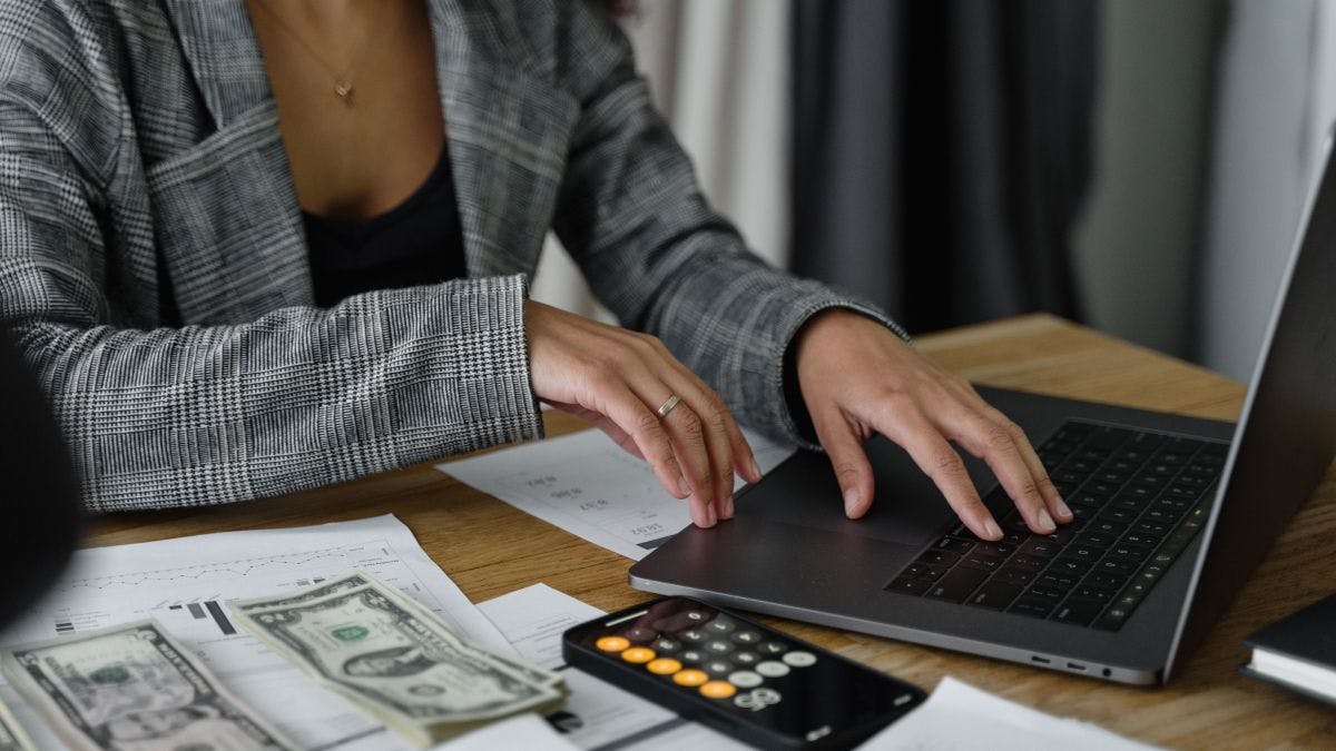 A person using a laptop with a calculator and money next to them. 