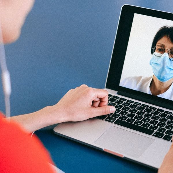 A person wearing a face mask and using a laptop for a video call. 