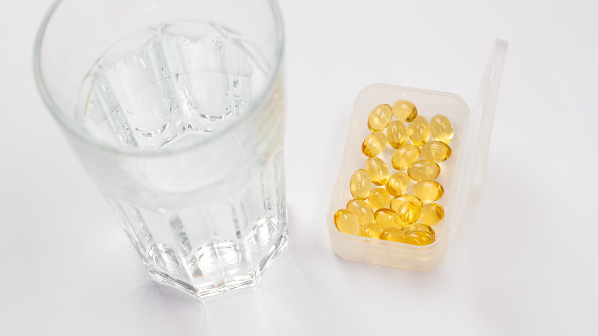A container of yellow pills next to a glass of water.