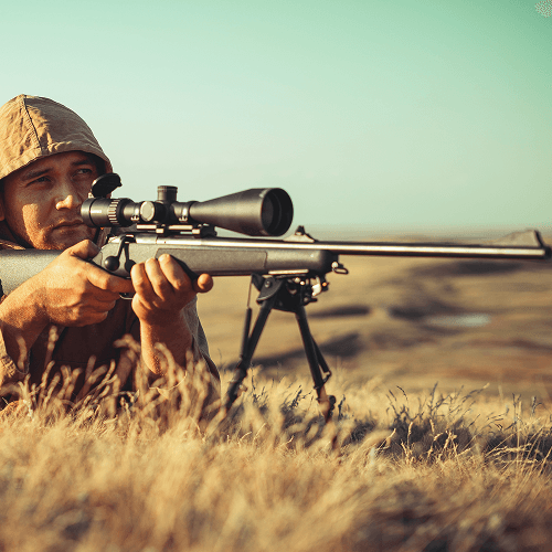 Background image of man prone in a field aiming down a rifle's sight