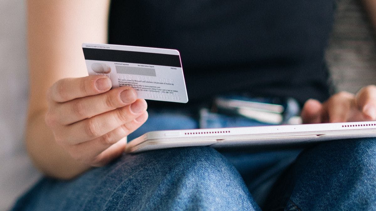 A person holding a credit card and a tablet.